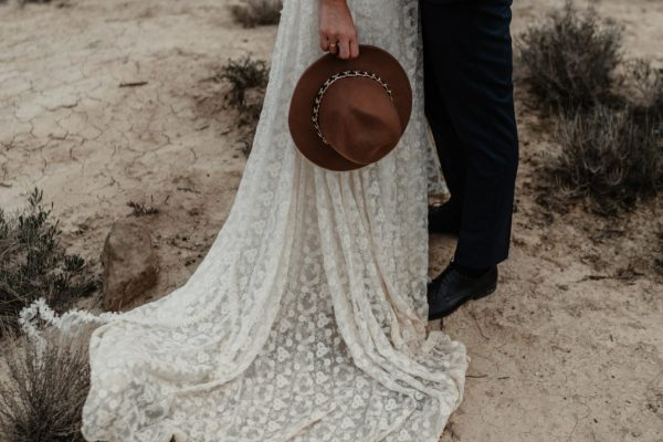 bride-holding-hat-groom-standing-near-bushes